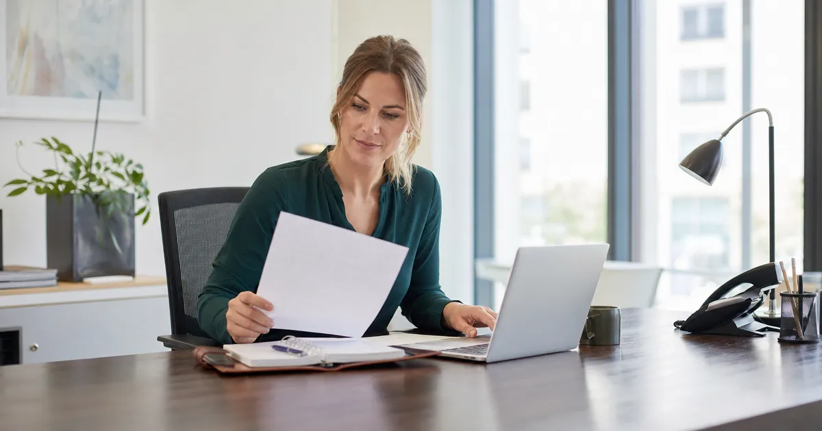 Officemanager schrijft een formele brief op een laptop, met een aanmaning en een klachtbrief op papier ernaast